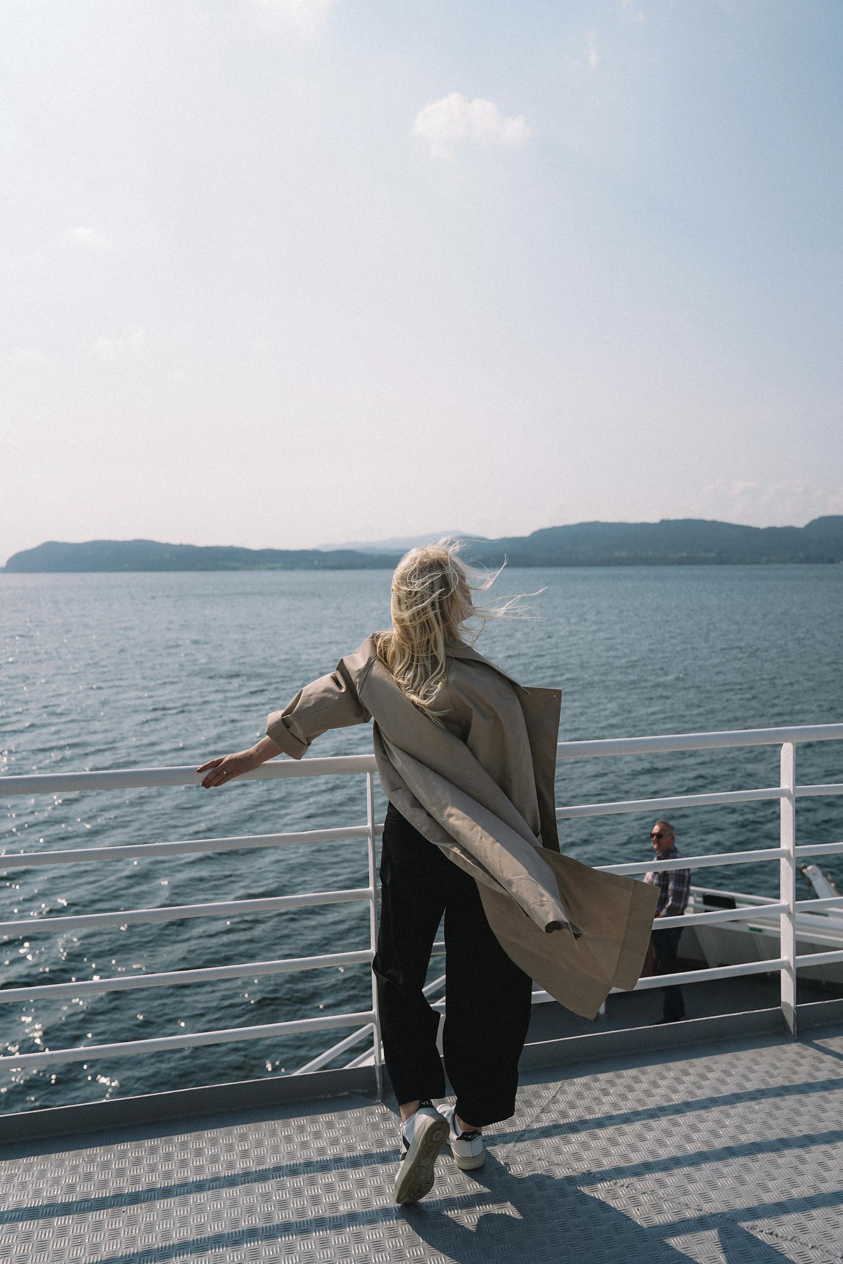A woman stands on a ferry overlooking the ocean, enjoying a serene moment of relaxation in Norway.